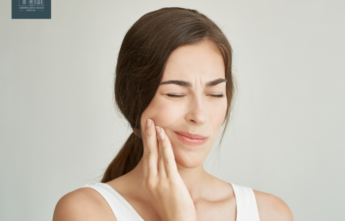 A female holding her hand up to her cheek. She is experiencing dental pain.